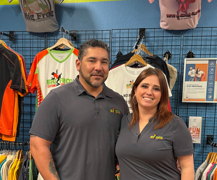 Josh and Tricia Lopez standing before the merchandising wall in the Big Frog store.