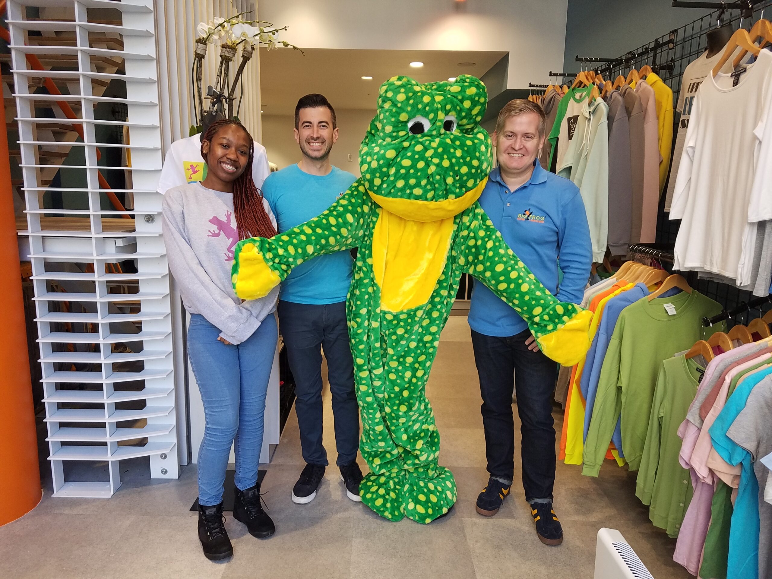 Big Frog Custom T-Shirts & More of The Upper West Side, Manhattan, New York store owners, Kerry Colley and Josh Drumm, standing with a female employee and a person wearing a Big Frog costume, inside the store