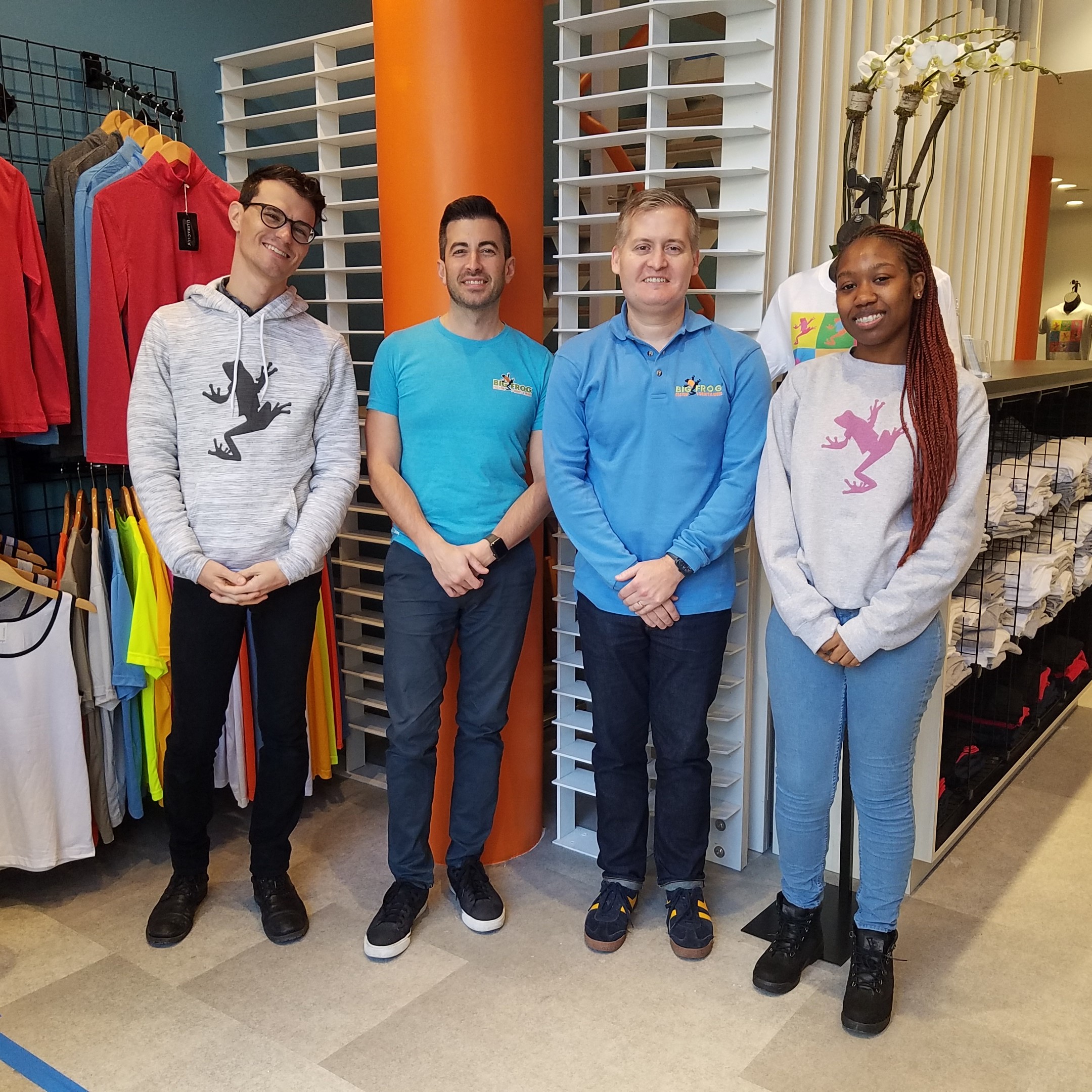 Big Frog Custom T-Shirts & More of The Upper West Side, Manhattan, New York team store owners Kerry Colley and Josh Drumm, standing with a male employee and a female employee inside the Big Frog store