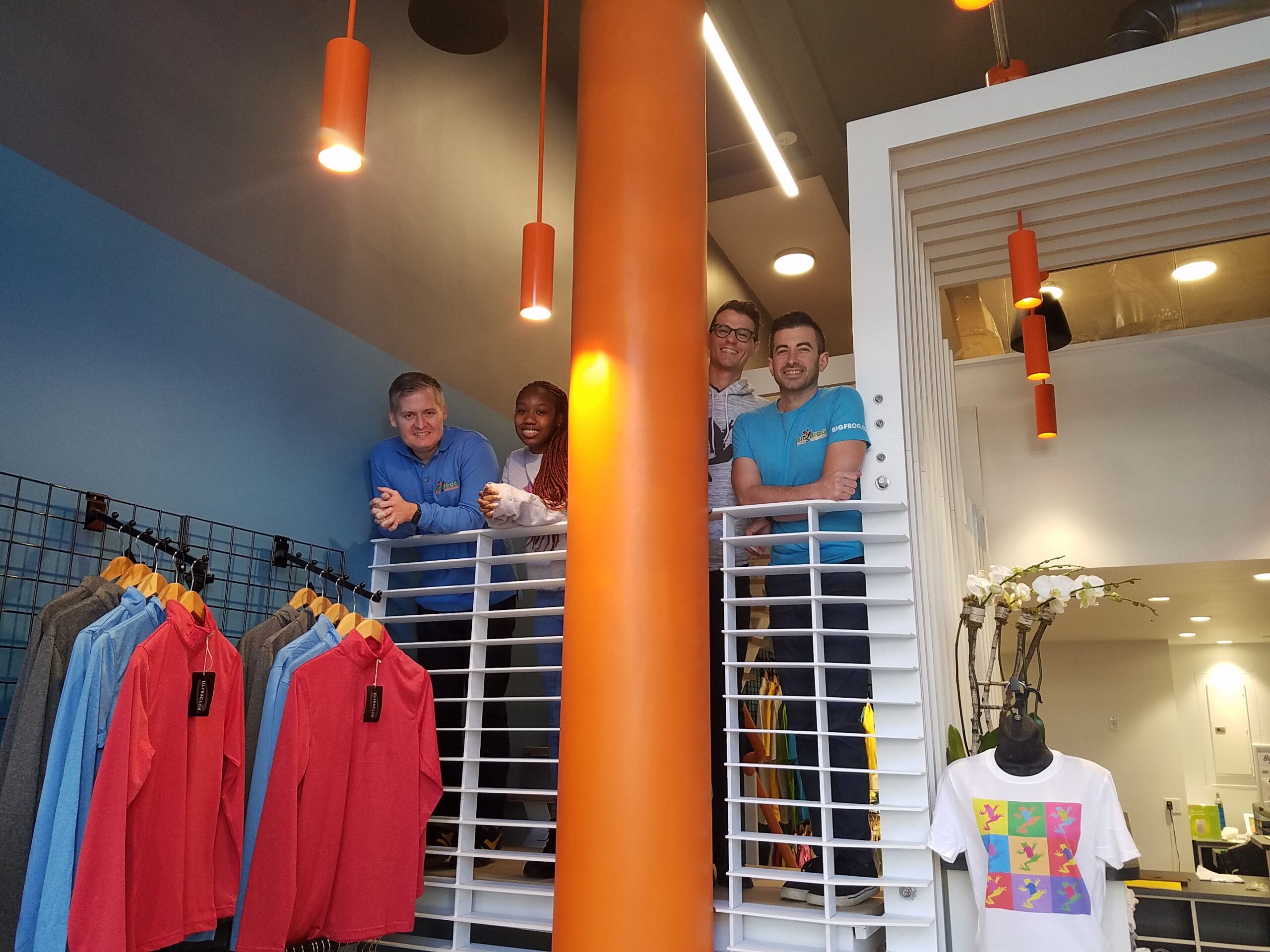 Big Frog Custom T-Shirts & More of The Upper West Side, Manhattan, New York store owners, Kerry Colley and Josh Drumm, standing upstairs and inside the Big Frog store, with a male employee and a female employee, overlooking the downstairs portion of the store.