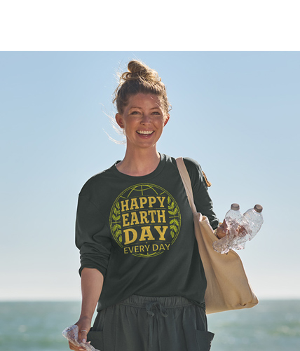 Image of blonde woman walking on the beach with empty water bottles in her hand. She is smiling and holding a tote bag